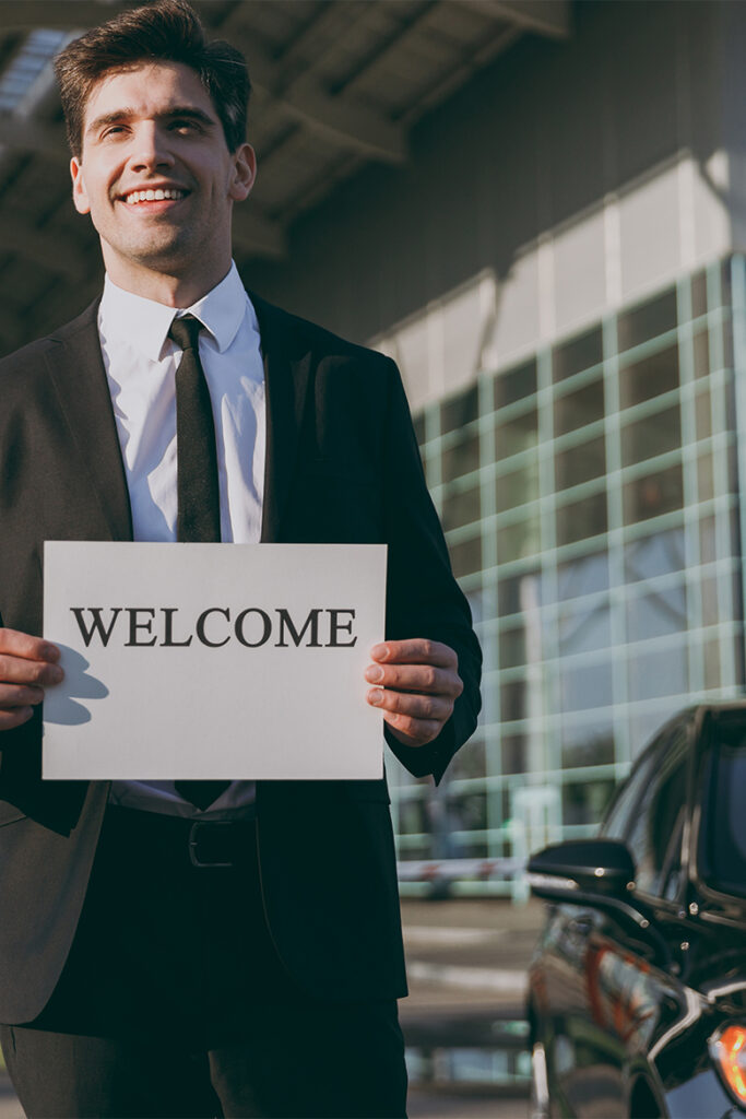 A chauffeur in a dark suit holding a welcome sign in an airport arrivals hall