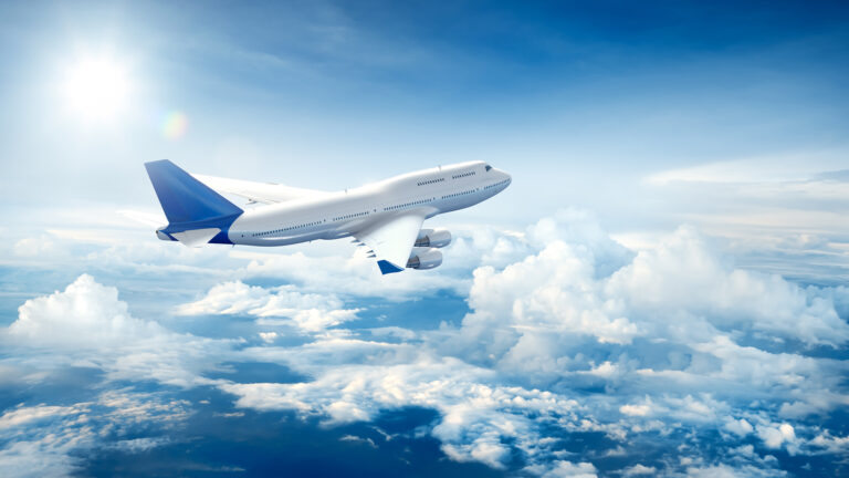 Airplane flying above fluffy clouds in a bright blue sky, symbolizing travel and adventure.