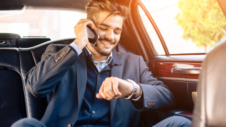 Businessman in a suit sitting in a luxury car, talking on the phone while checking his watch, exuding professionalism and confidence.