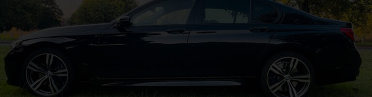 Black BMW sedan parked in a scenic outdoor setting, showcasing its sleek design and modern features. The image highlights the vehicle's stylish alloy wheels and polished exterior against a backdrop of greenery.