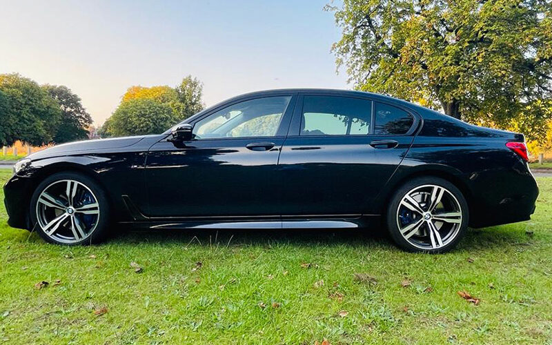 A black executive saloon parked on grass beneath trees
