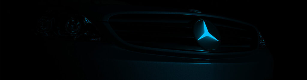 Close-up of a Mercedes-Benz car front grille featuring the illuminated three-pointed star emblem, set against a dark background, highlighting the vehicle's luxury design and branding.