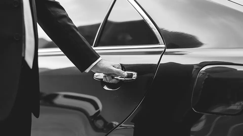 A business professional in a suit reaching for a car door handle, symbolizing luxury transportation and executive travel services.