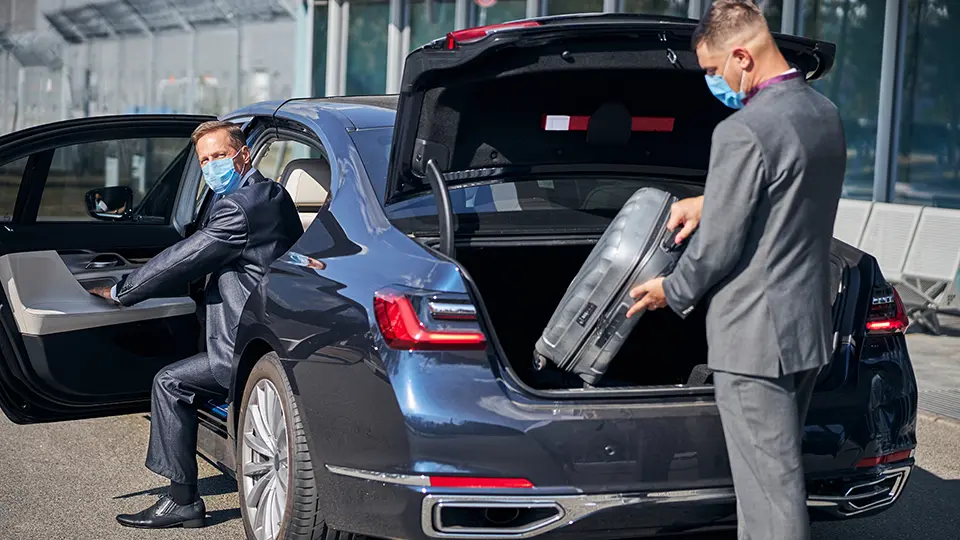 A passenger stepping into a chauffeur car outside a terminal