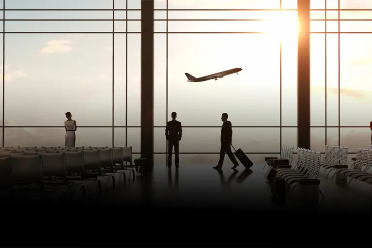 Silhouette of travelers in an airport terminal, with a plane taking off against a sunset backdrop and empty seating in the foreground.