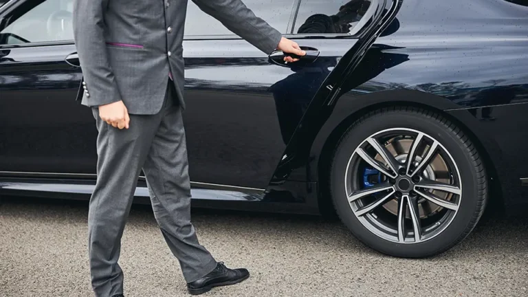 Businessman in a stylish suit opening the door of a luxury black car, showcasing modern automotive design and high-end features. The image highlights professional attire and the elegance associated with premium vehicles.