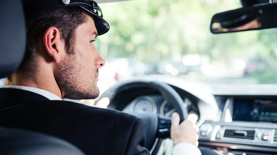A uniformed chauffeur driving with both hands on the wheel