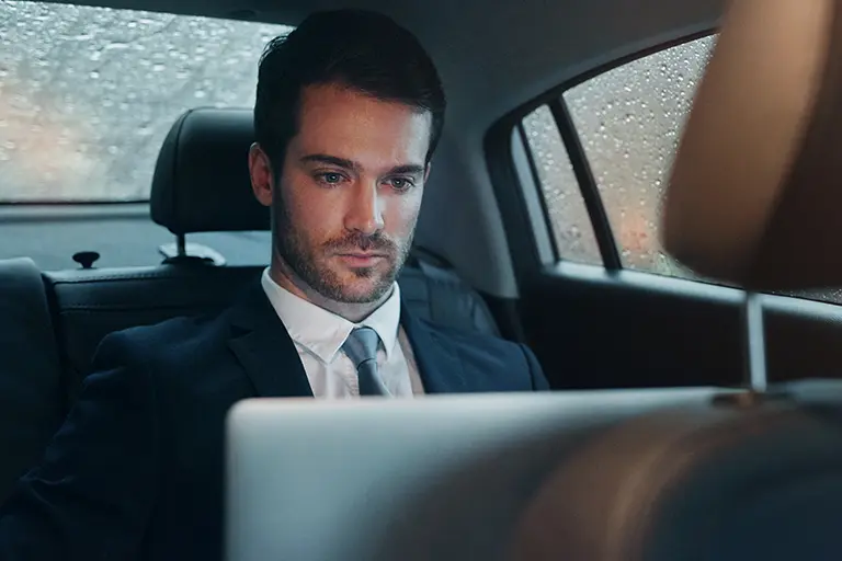 A passenger working on a laptop in the rear of a chauffeur-driven car