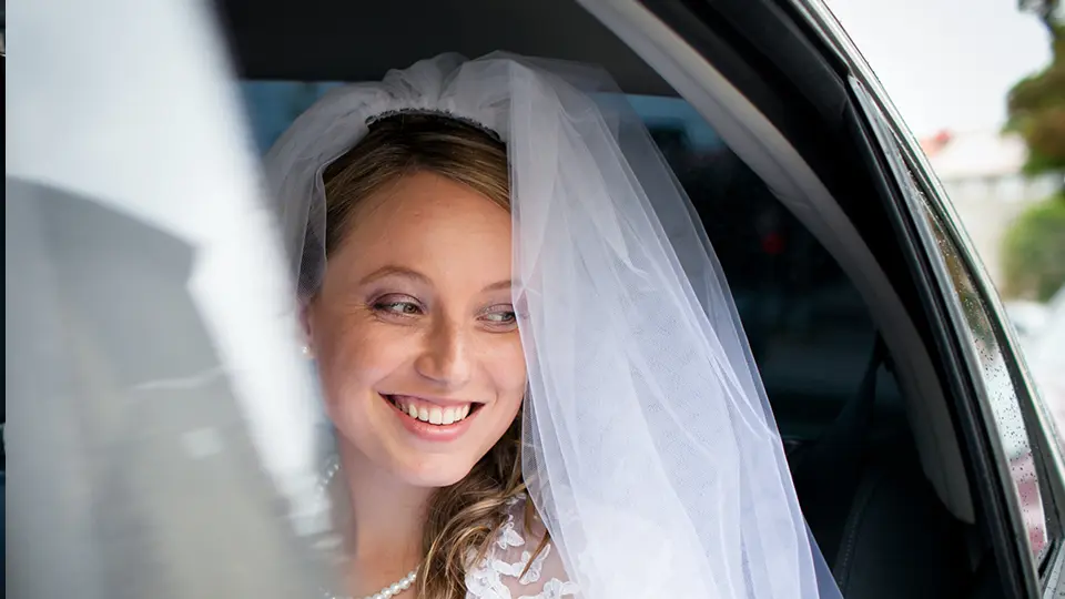 A bride in a wedding dress and veil in the rear of a car