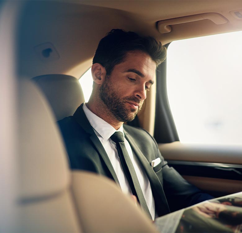 Business professional in a suit reading a magazine while seated in a luxury car, showcasing a sophisticated and modern lifestyle.