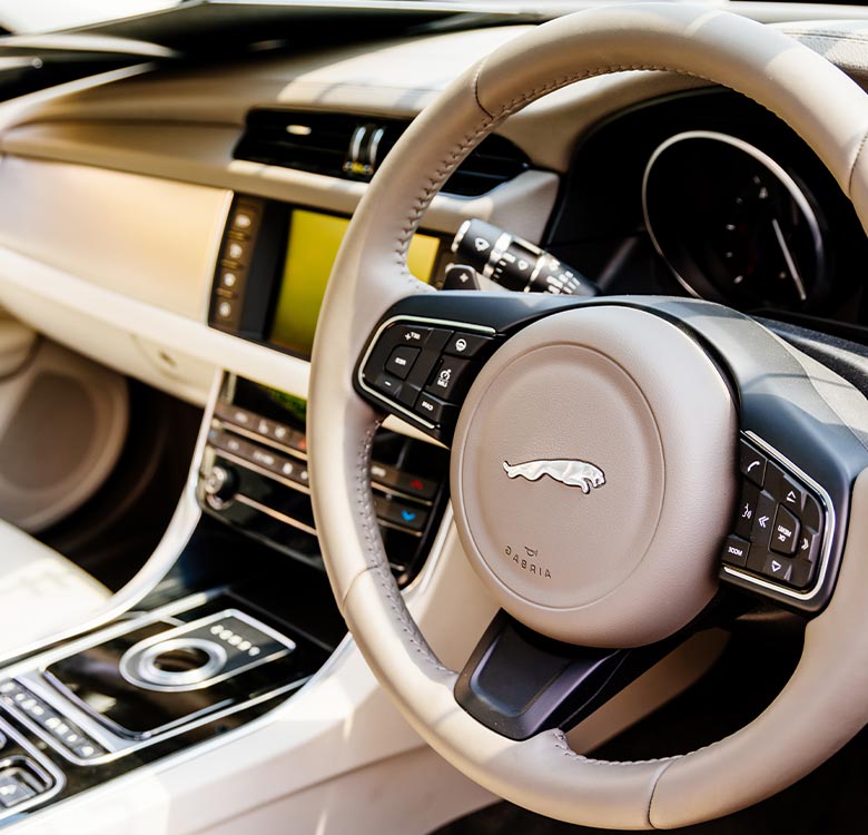 Close-up view of a Jaguar car interior featuring a sleek steering wheel with the Jaguar emblem, modern infotainment system, and polished console controls, emphasizing luxury and advanced technology in automotive design.