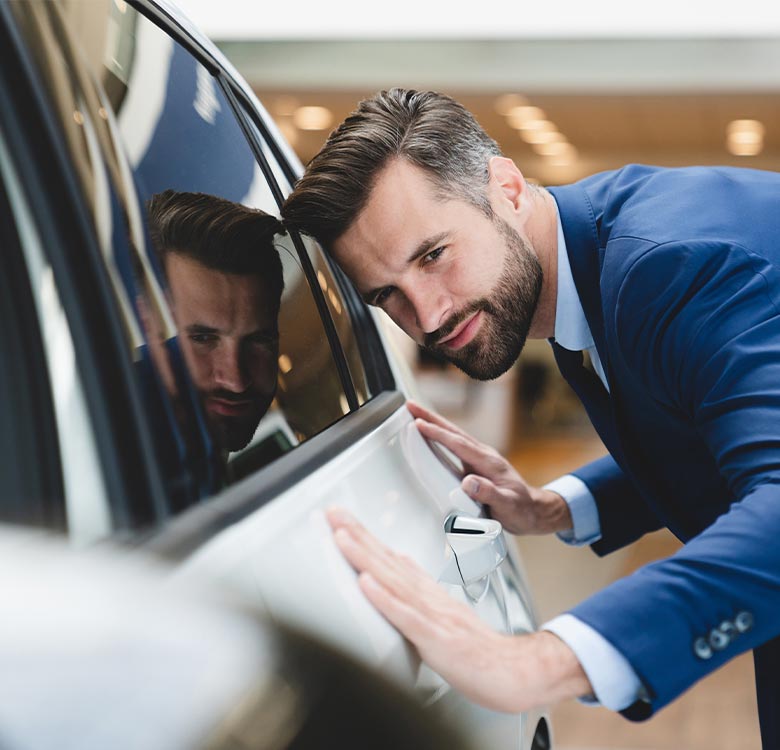 Businessman in a blue suit admiring a sleek white car, showcasing the vehicle's design and luxury features in a modern showroom setting.
