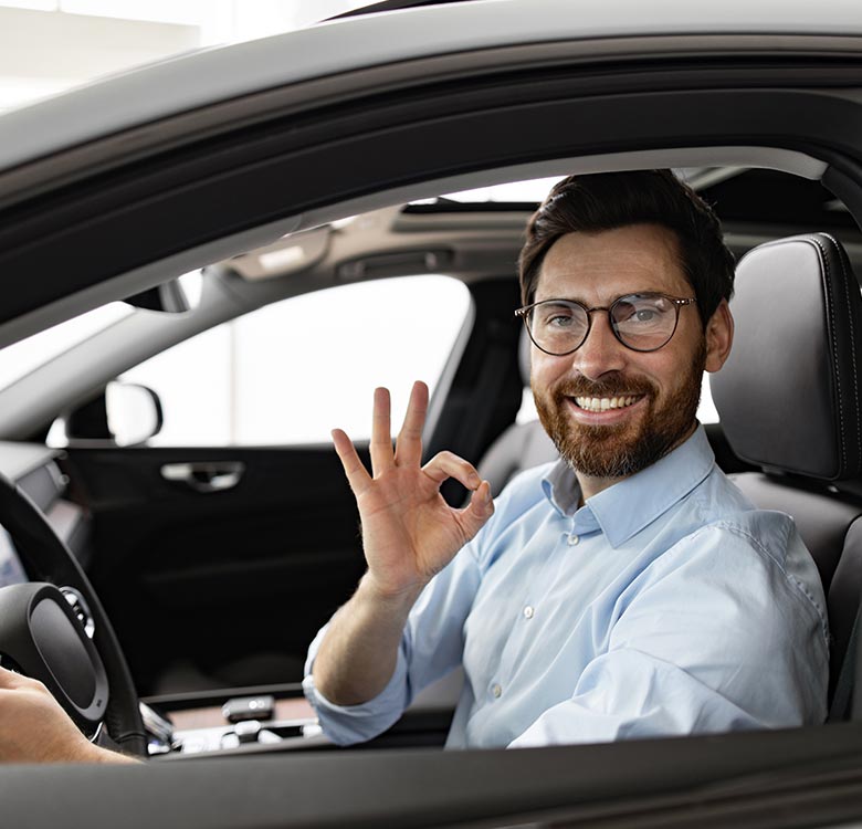 Man smiling in a car, showing an "okay" hand gesture, representing satisfaction and confidence in driving.