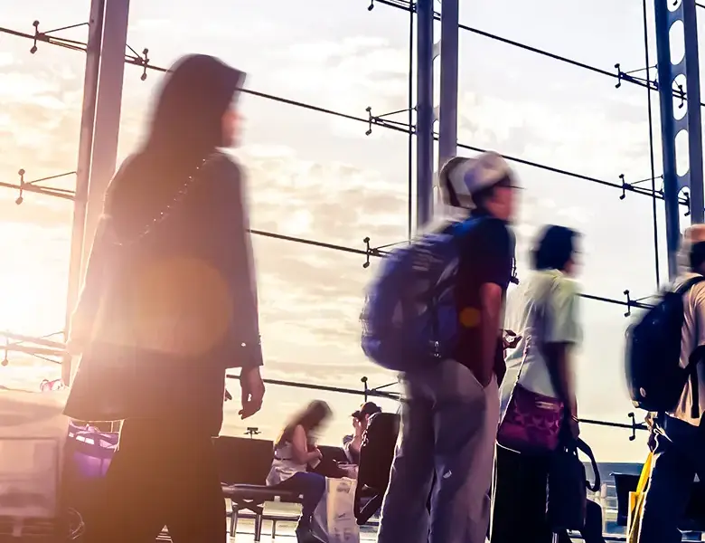 Blurred image of travelers walking through a modern airport terminal during sunset, showcasing busy movement and diverse travelers with backpacks and luggage.