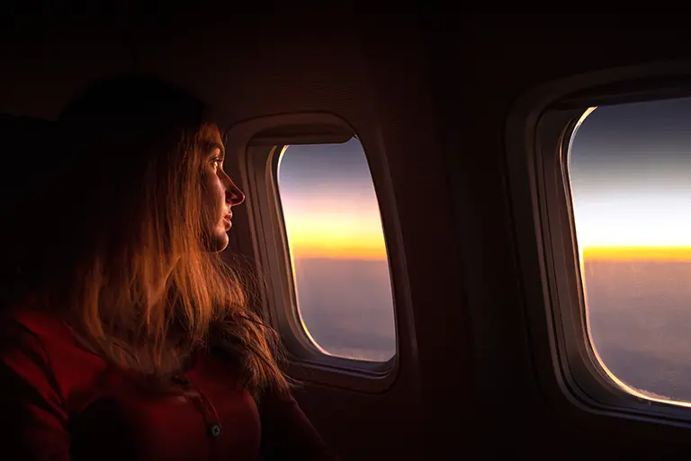 Young woman gazing out of an airplane window during sunset, capturing a moment of reflection and travel inspiration.