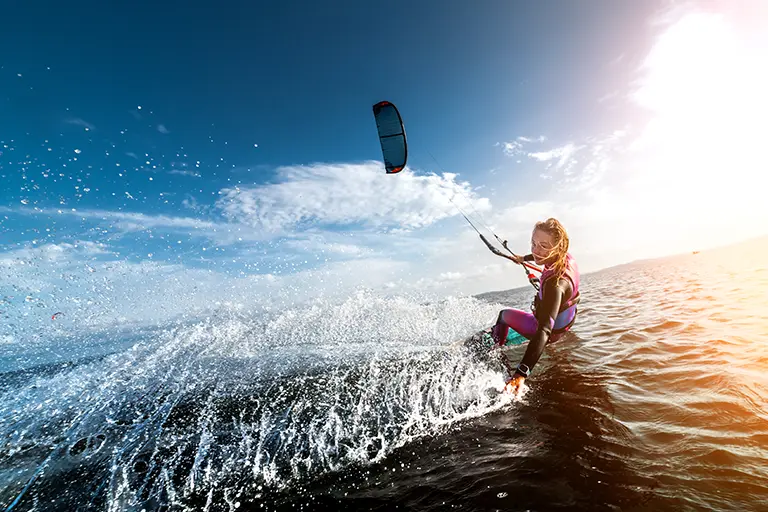 Kiteboarder performing tricks on a vibrant ocean during a sunny day, with splashes of water and a clear blue sky in the background.