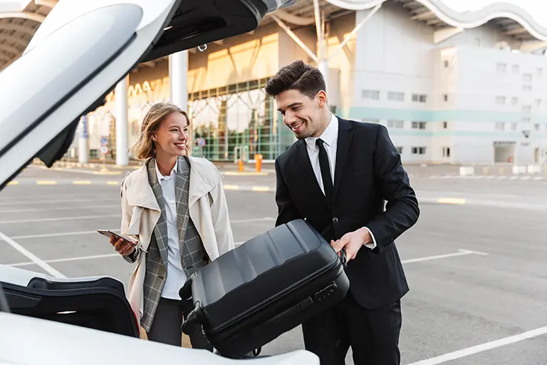 Business professionals loading luggage into a car trunk at an airport, showcasing travel readiness and modern business attire.